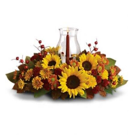 Madison Avenue Florist Sacramento - Symbolizing warmth and happiness, it is no wonder the sunflower is a quintessential ingredient in so many fall bouquets. This centerpiece maximizes the joy of sunflowers by arranging them with a bevy of fall flowers, foliage and a cranberry hued candle under hurricane glass.  Along with brilliant sunflowers, you'll find yellow spray roses, bronze and rust chrysanthemums, red berries, magnolia leaves and of course an elegant tapered candle inside a hurricane vase.  Approximately 21\