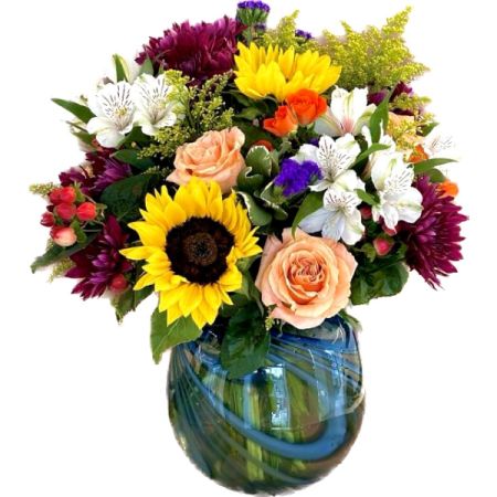 Conroy's Florist & Flower Delivery Mission Viejo - Swirling Elegance: Artistry in Bloom" is a magnificent floral arrangement that resides in an exquisite art glass vase adorned with mesmerizing blue swirls. This masterpiece of floral design, meticulously crafted by a highly skilled floral designer, combines the timeless beauty of sunflowers, the romantic allure of roses, the delicate charm of solidaster, and the enduring elegance of chrysanthemums.