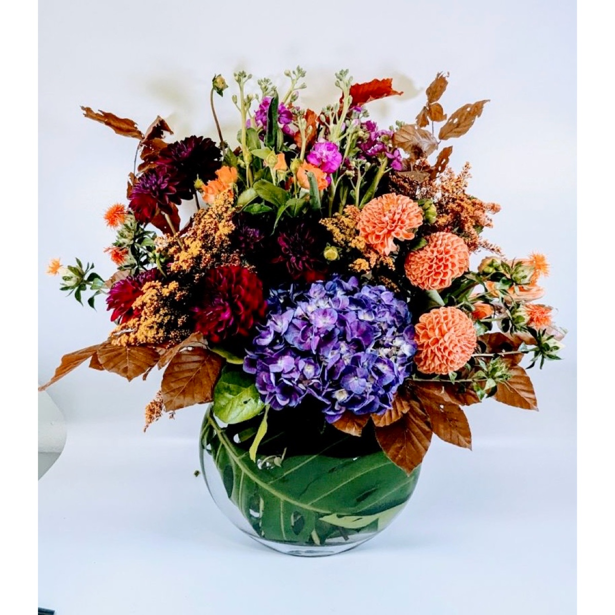 Conroy's Florist & Flower Delivery Mission Viejo - This stunning arrangement, “Harvest Symphony” is custom designed for our Fall Collection. The rich, harmonious blend of deep purples, vibrant oranges, and soft peach tones evokes the beauty of a bountiful autumn harvest, enhanced by the natural textures of the leaves and blooms.
