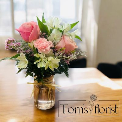 Tom's Florist Smyrna - Sweet, simple, and full of charm, Tickled Pink is a one-sided arrangement that’s perfect for delivering a dose of joy—no matter the occasion. Designed in a pink mason jar and finished with a rafia bow, this arrangement is as cute as it is thoughtful.

A cheerful blend of pink roses, pink carnations, pink wax flower, white alstroemeria, and lavender limonium creates a soft, playful palette with just the right touch of whimsy. Its compact size makes it ideal for desks, side tables, or anywhere you want to add a little sunshine.

Whether you're celebrating a milestone or simply sending smiles, Tickled Pink is a delightful reminder that the prettiest gestures come in small packages.