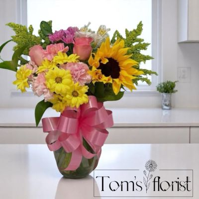 Tom's Florist Smyrna - Bring a burst of happiness to someone’s day with “You Are My Sunshine,” a vibrant arrangement full of charm, color, and heartfelt cheer. This radiant bouquet features a standout sunflower at its center, surrounded by sweet pink carnations, soft pink roses, crisp white alstroemeria, sunny yellow daisies, and golden touches of solidago.

The combination of yellow and pink blooms creates a joyful, uplifting palette that’s perfect for celebrating birthdays, expressing gratitude, or simply reminding someone how much they brighten your life.

Fresh, playful, and full of positive energy, “You Are My Sunshine” is a floral hug in bloom—guaranteed to make them smile.
