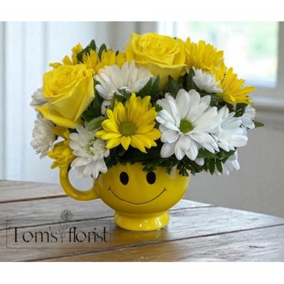 Tom's Florist Smyrna - Bring a burst of joy to someone's day with our Sunshine Smiles Bouquet. This cheerful arrangement features a lovely mix of white and yellow roses and daisies, carefully arranged to brighten any room. Presented in a playful yellow smiley face mug, this delightful floral display is the perfect way to spread happiness and positivity. Whether you're celebrating a special occasion or simply sending a smile, this arrangement is sure to lift spirits and warm hearts.