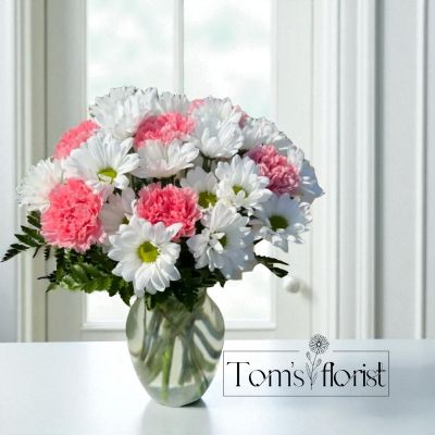 Tom's Florist Smyrna - Bring a burst of joy to any occasion with our delightful Pink Posey! This charming bouquet features the pure simplicity of fresh white daisies, perfectly complemented by the soft, sweet hues of pink carnations. Whether you're celebrating a birthday, sending well wishes, or just brightening someone's day, this arrangement is sure to bring a smile. The cheerful combination of these blooms creates a light, airy feel that's as heartwarming as a hug. Add a touch of happiness with the Pink Posey – the perfect way to share love and sunshine in a vase!