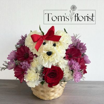 Tom's Florist Smyrna - Talk about puppy love! Crafted from lasting white carnations, our canine cutie is sitting pretty in a dog bed basket, surrounded by a mix of red, lavender and purple blooms. The perfect pick to spark romance or celebrate a special relationship. One-sided 3D arrangement with white carnations, red roses & mini carnations, purple & lavender daisy poms; accented with assorted greenery Crafted in the shape of a dog, complete with eyes, nose and red satin ribbon Artistically designed in our lined wicker pet basket, arrangement measures approximately 11"H x 11"W. Our florists hand-design each arrangement, so colors, varieties and container may vary due to local availability






