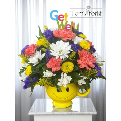Tom's Florist Smyrna - Brighten someone’s day with a burst of happiness! Sending Smiles is a cheerful arrangement designed to lift spirits and spread joy. Presented in an adorable yellow smiley face mug, this bouquet is a perfect way to say "thinking of you," "get well soon," or simply "just because."

This colorful mix includes:

White daisies for innocence and cheer

Vibrant orange carnations for warmth and admiration

Sunny yellow button poms for a playful pop

Rich purple statice for depth and contrast

Golden solidago to tie it all together

Once the flowers have faded, the smiley face mug doubles as a fun keepsake—ideal for coffee, tea, or a daily dose of happiness!

Perfect for: Get well wishes, birthdays, thank-you gifts, or anytime someone could use a smile.