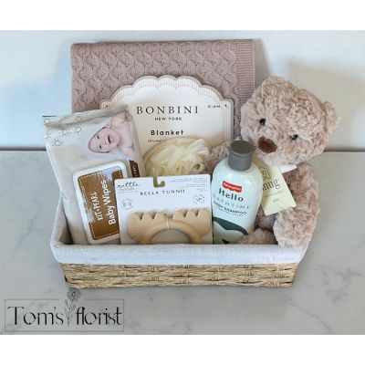 Tom's Florist Smyrna - The Softest Welcome Gift Basket is a beautifully curated collection of essentials and sweet keepsakes for newborns and their families. With soft textures, neutral tones, and baby-safe care items, this basket is designed to bring comfort, practicality, and joy to baby's first days.

What’s included:

Neutral Color Teddy Bear
A soft and cuddly companion perfect for snuggles, photo ops, and nursery decor.

Luffa Sponge
A natural, gentle sponge ideal for baby’s bath time routine.

Fisher-Price Baby Shampoo (10 fl. oz)
Hypoallergenic and tear-free, this gentle shampoo is perfect for sensitive scalps and daily use.

Bonbini Blanket (38" x 28")
Sized for 0–6 months, this cozy, lightweight blanket is perfect for swaddling or stroller rides.

Bella Tunno Rattle Teether
A dual-purpose teether and rattle that soothes gums and entertains little hands, made with baby-safe materials.

Kit + Pearl Baby Wipes
Hypoallergenic wipes made for the most delicate skin—perfect for diaper changes and on-the-go cleanups.