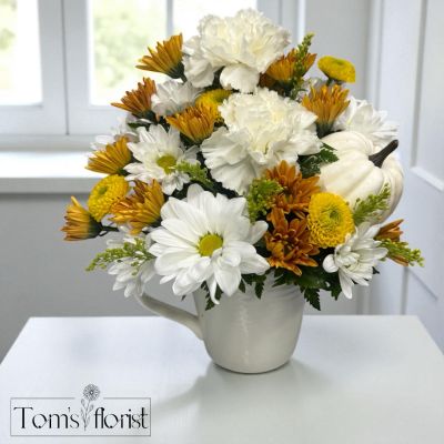 Tom's Florist Smyrna - A simple touch of fall charm — this white ceramic mug is filled with soft seasonal blooms in warm, inviting tones. Its clean, minimal look makes it the perfect accent for a cozy desk, coffee nook, or side table. Subtle, sweet, and effortlessly autumn.
