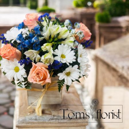 Tom's Florist Smyrna - Inspired by the soothing shades of a seaside retreat, our popular bouquet will bring its tranquil beauty to someone special. Artistically designed in our grey-washed wooden cube featuring soft, natural tones and textures, it’s finished with a touch of raffia to deliver your sentiments in cool, summery style. One-sided arrangement with peach roses, blue delphinium, white Peruvian lilies (alstroemeria) and daisy poms, purple statice; accented with assorted greenery Artistically designed in our exclusive grey washed wooden cube tied with raffia; features a rustic style and natural, textural beauty; measures 5.2"L x 5.2"H x 5.2"W Our florists hand-design each arrangement, so colors and varieties may vary due to local availability To ensure lasting beauty, Peruvian lilies may arrive in bud form and will fully bloom over the next few days