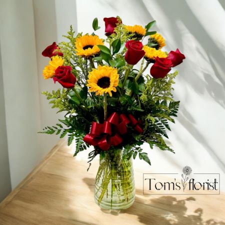 Tom's Florist Smyrna - Make a bold statement with Romance Reimagined, a grand and stunning floral arrangement that perfectly blends passion and vibrancy. This breathtaking design features luxurious red roses symbolizing deep love, bright sunflowers radiating warmth and joy, and delicate solidago for a touch of elegance. Expertly arranged to create a show-stopping centerpiece, Romance Reimagined is the ideal gift for anniversaries, romantic occasions, or any moment when you want to express your love in an unforgettable way. Let this striking bouquet bring a touch of sophistication and charm to your celebration of love.