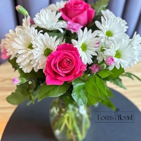Tom's Florist Smyrna - Brighten any space with Hello Gorgeous, a lively and joyful floral arrangement that combines the freshness of white daisies with the vibrant energy of hot pink roses and mini carnations. The soft white daisies offer a touch of simplicity, while the bold pink hues bring a pop of fun and warmth to this captivating design.

Perfect for adding a cheerful accent to any occasion, Hello Gorgeous is a celebration of love, joy, and beauty. Whether as a gift for someone special or a vibrant centerpiece for your home, this arrangement will bring smiles and a burst of color to all who see it.