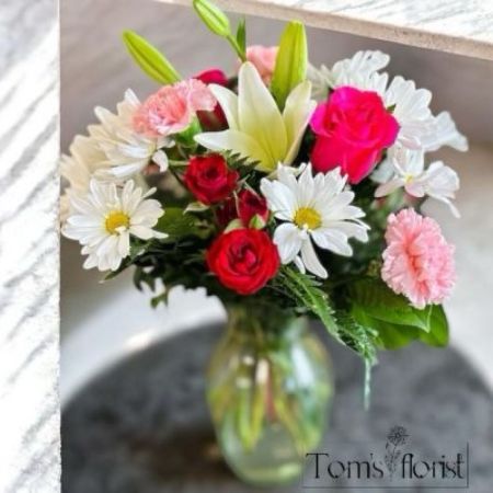 Tom's Florist Smyrna - Step into a world of color with Fuchsia Fantasy, a dazzling floral arrangement that combines the pure elegance of white daisies with the bold energy of hot pink roses and mini carnations. This playful yet sophisticated design offers a striking contrast of bright hues, creating an irresistible burst of joy and cheerfulness.

Perfect for brightening up any occasion or adding a lively touch to your space, Fuchsia Fantasy is a celebration of color, beauty, and vibrant energy. Whether you're gifting it to someone special or treating yourself, this arrangement is sure to captivate and bring smiles wherever it goes.