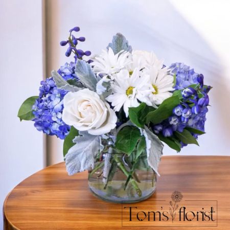 Tom's Florist Smyrna - A harmonious blend of blue hydrangeas and delicate white blooms, Blue Moon Blossoms exudes tranquility and grace. The soft blue hues of the hydrangeas paired with the purity of white flowers create a peaceful, timeless beauty. This elegant arrangement is thoughtfully designed to suit any occasion with subtle elegance. 