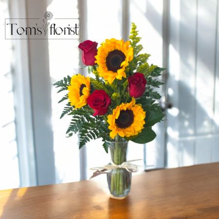 Tom's Florist Smyrna - Radiate warmth and passion with Sun Kissed Love, a vibrant bouquet that speaks straight from the heart. Featuring cheerful sunflowers, classic red roses, and golden solidago, this stunning arrangement is a bold blend of sunshine and romance.

Whether you're celebrating a love that lights up your world or sending a joyful surprise "just because," Sun-Kissed Love is the perfect way to brighten someone’s day with color, charm, and heartfelt emotion.