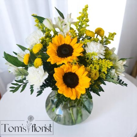 Tom's Florist Smyrna - Sunflower Dreams is a cheerful, golden-hued arrangement designed to bring warmth and positivity to any space. Featuring radiant sunflowers as the focal point, this sunny bouquet is complemented by crisp white alstroemeria, soft white carnations, playful yellow button poms, and golden accents of solidago.

This dreamy mix of blooms evokes the gentle beauty of a late summer morning—fresh, hopeful, and full of light. Whether you’re celebrating a special occasion or simply sending a little sunshine someone’s way, Sunflower Dreams is the perfect floral escape.

Let joy bloom with this heartfelt and luminous arrangement.


