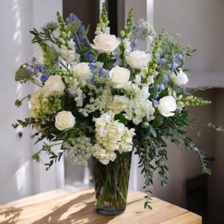 Tom's Florist Smyrna - Celebrate life’s most special moments with Grand Embrace, a lush and elegant floral arrangement designed to captivate and inspire. Featuring pristine white roses, cloud-like hydrangeas, and tall, graceful delphinium, this stunning display brings a sense of beauty, serenity, and refinement to any space. Perfect for welcoming a new arrival, marking a milestone, or simply brightening someone’s day, Grand Embrace is a timeless statement of thoughtfulness and luxury.