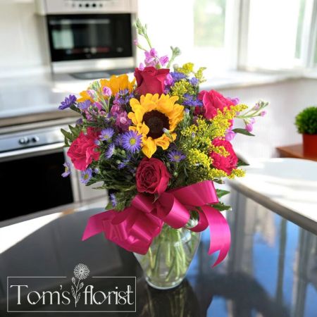 Tom's Florist Smyrna - Turn up the color with Bold Blossoms—a lively, joyful arrangement bursting with personality. Featuring sunny sunflowers, vibrant hot pink roses and carnations, rich purple monte, and cheerful yellow solidago, this bouquet is designed to brighten any space and every mood. Perfect for celebrations, thank-yous, or just because, Bold Blossoms brings the energy of a blooming summer garden into any room.

Available for in-store pick- up or local delivery in Smyrna, La Vergne, Antioch, Nolensville, and Murfreesboro.