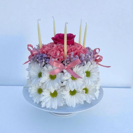 Tom's Florist Smyrna - A charming floral “cake” made with fresh white daisies, soft pink carnations, delicate purple baby’s breath, and crowned with a single romantic rose. Topped with slender candles, it’s the perfect bouquet to celebrate any birthday—blow out the (imaginary) candles and let the flowers steal the show!