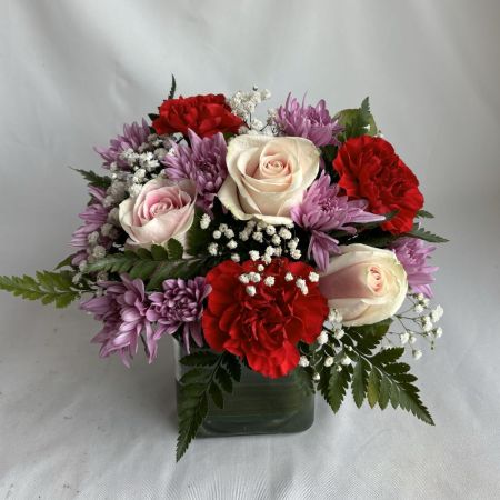 Conroy's Flowers San Diego San Diego - A sumptuous arrangement of blush roses, ruby carnations, and soft lavender blooms, accented with baby’s breath and lush greenery. Gracefully styled in a modern glass cube, this design radiates refined romance and effortless luxury.