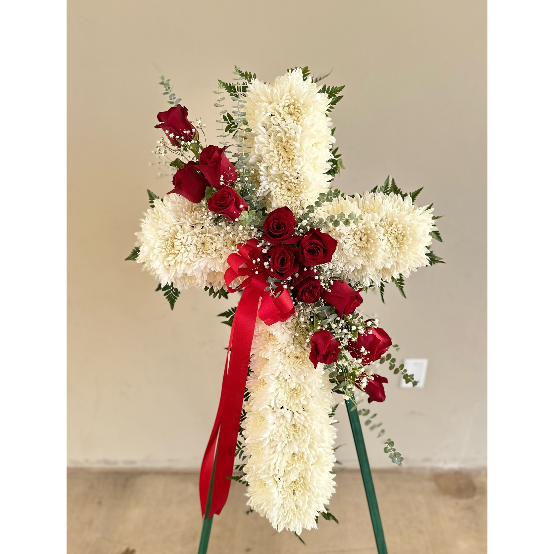 Conroy's Flowers El Cajon El Cajon - Embrace the comfort of faith and honor the memory of your loved one with our Peace & Prayers™ Red & White Standing Cross. Expertly handcrafted by our florists, this unique arrangement features a bed of white mums meticulously arranged in the shape of a cross. Accentuated with a cascade of vibrant red roses and delicate spiral eucalyptus, the floral tribute is a beautiful expression of love and sympathy. It serves as a special way for the family to offer peace and comfort during the challenging moments of loss.