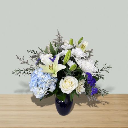 Blooms of Wayne Wayne - Beautiful in Blue is a serene blue and white floral arrangement featuring roses, lilies, and hydrangea in a modern blue vase. Perfect for sympathy, appreciation, or elegant everyday gifting with same-day delivery available.