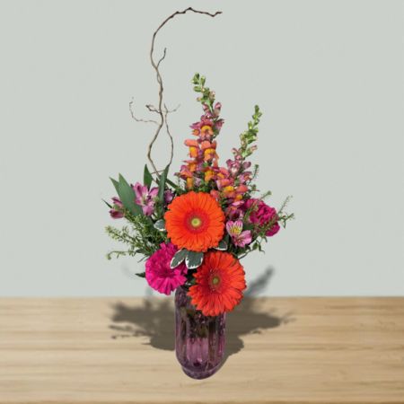 Blooms of Wayne Wayne - Bring the warmth of the islands into any space with our 'Tropical Delight' bouquet—a vibrant burst of color and texture. 
Rich fuchsia roses and fiery orange gerbera daisies dance amongst lush greenery and delicate stock, evoking a sense of exotic escape.
Presented in a uniquely textured, keepsake, glass vase, this stunning floral arrangement is perfect for brightening a home or celebrating a special occasion.
Send a little sunshine and joy with this unforgettable gift of fresh tropical flowers, guaranteed to uplift and inspire.