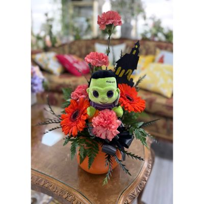 DiBella Flowers & Gifts Las Vegas - Bring a playful touch of spooky charm to your Halloween décor with the Frankenstein Bowl! Featuring bright orange gerbera daisies and cheerful carnations arranged in a festive pumpkin-style container, this arrangement is topped off with a cuddly Frankenstein plush for extra fun. Accented with lush greenery, a black satin bow, and a haunted house detail, it’s the perfect centerpiece for Halloween parties, a gift for kids, or a spirited way to brighten someone’s day.