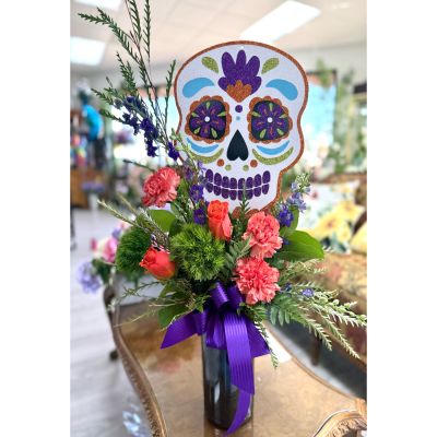 DiBella Flowers & Gifts Las Vegas - Bold, bright, and full of personality, the Skullflower Surprise Arrangement brings festive flair to any space. A glittering skull rises above a cheerful mix of roses, carnations, greenery, and vibrant purple accents, tied together with a rich purple bow. This playful design is perfect for celebrating life, love, and tradition with a colorful twist.   