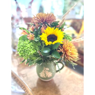 DiBella Flowers & Gifts Las Vegas - This charming arrangement radiates cozy countryside elegance, featuring a bright golden sunflower at its heart. Soft rust-toned mums, peachy alstroemeria, and lush green hydrangea add rich texture and depth, while wisps of wheat give it a touch of rustic harvest charm. Designed in a vintage-style sage green pitcher, it feels like a cheerful bouquet gathered fresh from a sunlit meadow—perfect for brightening any home with warmth and natural beauty.