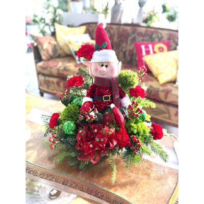 DiBella Flowers & Gifts Las Vegas - This festive arrangement features a cheerful elf nestled among lush winter greens, bright red blooms, berries, and sparkling holiday accents, bringing playful North Pole charm and merry color to any space. 