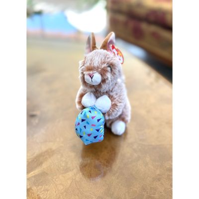 DiBella Flowers & Gifts Las Vegas - Praline is a soft brown bunny with cuddly fur and big sparkly eyes. She holds a bright blue Easter egg, adding a festive and playful touch to her sweet look. Perfect for springtime fun and cozy snuggles.