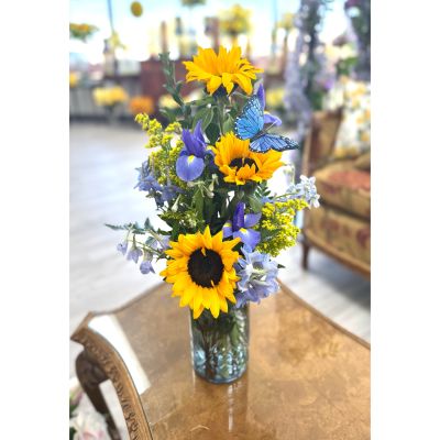 DiBella Flowers & Gifts Las Vegas - Make a bold, uplifting statement with this vibrant sunflower and blue floral arrangement, designed to turn heads and lift spirits. Featuring golden sunflowers, cool blue blooms, and a whimsical butterfly accent, this piece is perfect for Mother's Day, birthdays, celebrations, or just because. Available for same day Las Vegas flower delivery or convenient pickup, each arrangement is handcrafted by DiBella Flowers and gifts for a fresh, memorable gift experience.