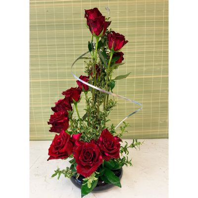Uptown Blossoms Anchorage - A captivating dance of deep red roses, gracefully spiraling upwards amidst lush greenery, creates a stunning focal point for any space. This modern rose arrangement, perfect for expressing passionate love or heartfelt admiration, exudes both elegance and romance. 'Spiral Roses' arrive in a chic vessel, ready to bring a touch of sophisticated beauty to a birthday, anniversary, or simply to brighten someone’s day. Send the gift of enduring affection with this unforgettable bouquet of fresh, vibrant roses.