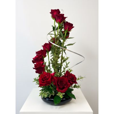 Uptown Blossoms Anchorage - A captivating dance of deep red roses, gracefully spiraling upwards amidst lush greenery, creates a stunning focal point for any space. This modern rose arrangement, perfect for expressing passionate love or heartfelt admiration, exudes both elegance and romance. 'Spiral Roses' arrive in a chic vessel, ready to bring a touch of sophisticated beauty to a birthday, anniversary, or simply to brighten someone’s day. Send the gift of enduring affection with this unforgettable bouquet of fresh, vibrant roses.