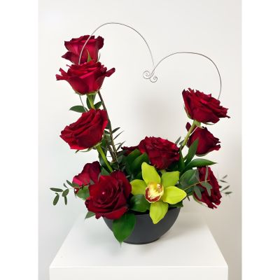 Uptown Blossoms Anchorage - Express your deepest affection with our Valentine Dozen with Orchids, a stunning bouquet of velvety red roses and exotic blooms. 
Deep crimson petals unfurl around graceful orchids, creating a captivating fragrance and a touch of modern elegance. 
Presented in a chic black vase and accented with lush greenery, this arrangement speaks volumes on its own.
Send a lasting symbol of love this Valentine's Day with this unforgettable dozen roses gift, perfect for that special someone. 