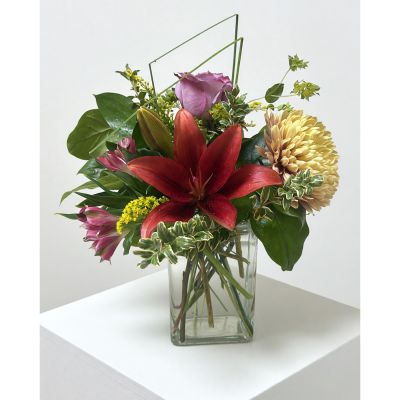 Uptown Blossoms Anchorage - Brighten any space with ‘Uptown Desktop Modern Mix’, a cheerful burst of color and texture in a stylish glass vase. 
Sun-kissed yellow lilies and a warm peach rose mingle with delicate purple chrysanthemums and sprigs of fresh greenery. 
This compact, contemporary arrangement sends a little sunshine, perfect for a desk, bedside table, or as a 'just because' gift.
Experience the joy of fresh flowers – order your beautiful desktop bouquet today for instant elegance and lasting happiness!