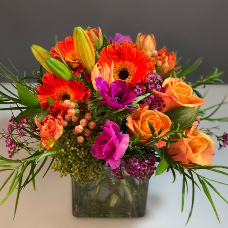 Bouquets Denver - Bright and vibrant this beauty crushes it with orange daisies and roses. Accented with Fuchsia blossoms or wax flower and anemones. 