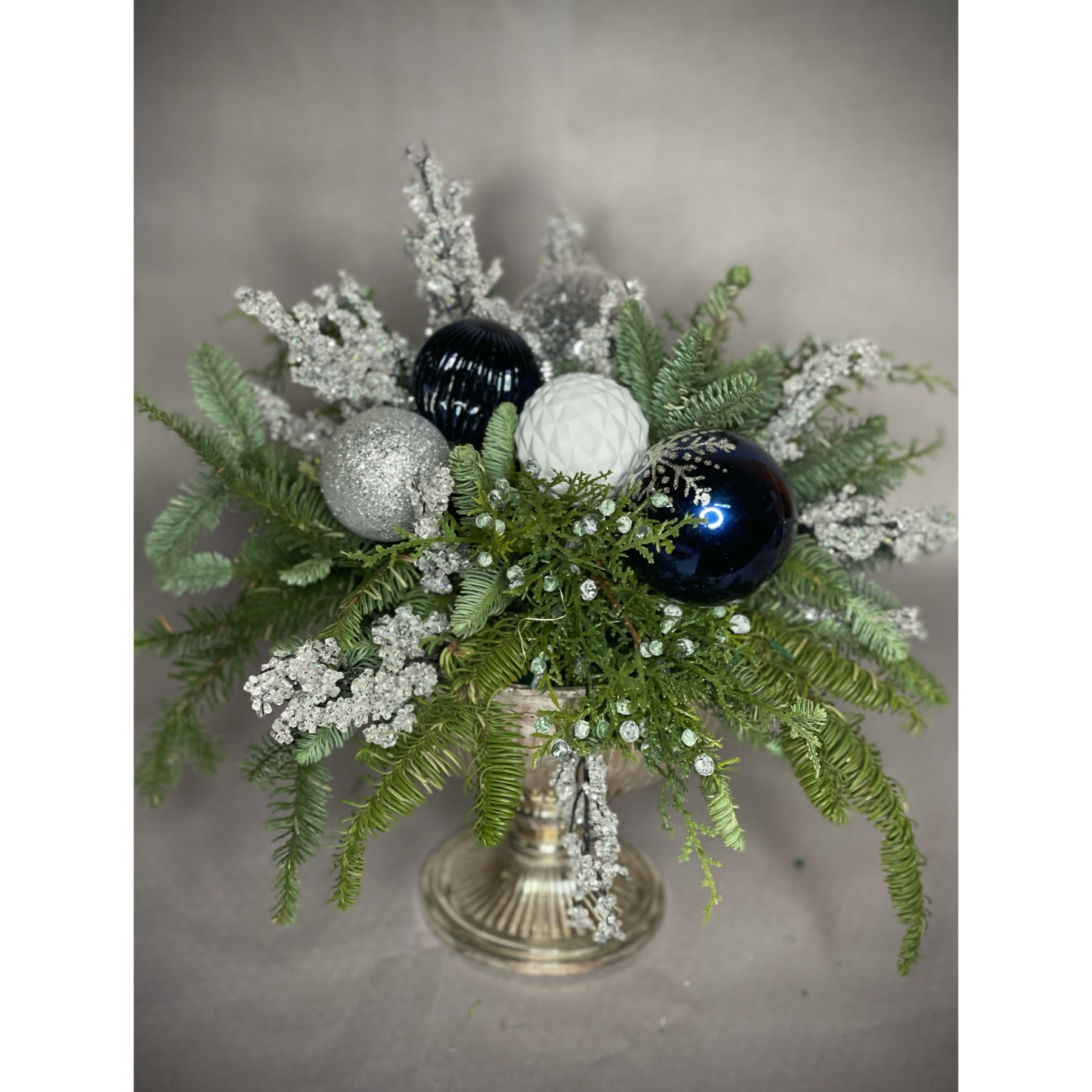 Bouquets Denver - Celebrate the season with a wonderful arrangement featuring evergreens and holiday balls adorned with faux ice crackles, all assembled in a silverplate metal footed urn. Opt for an upgrade with fresh blossoms to add a burst of natural beauty to the ensemble. Enjoy the convenience of same-day flower delivery, ensuring your festive display graces your space promptly. This charming combination of greenery and holiday accents brings a touch of winter magic to your surroundings. Elevate the elegance of your decor with the option to include vibrant fresh blossoms for an extra layer of festive cheer. Make a statement with this delightful arrangement that captures the spirit of the holidays.