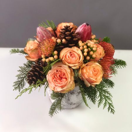 Bouquets Denver - Adorn your space with a captivating blend of evergreens, pincushion protea, pink ice protea, salmon-colored roses, hypericum berries, and pine cones in a charming white birch container. This exquisite arrangement adds a touch of natural beauty and seasonal charm to any setting. Enjoy the convenience of same-day flower delivery, ensuring your space is graced with this delightful display promptly. Embrace the unique combination of textures and colors, creating a visually stunning focal point. Elevate your decor with the enchanting allure of this carefully curated botanical ensemble.






